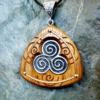 Classic Handmade Triskele Necklace in fine pewter on Iroko with background of spirals